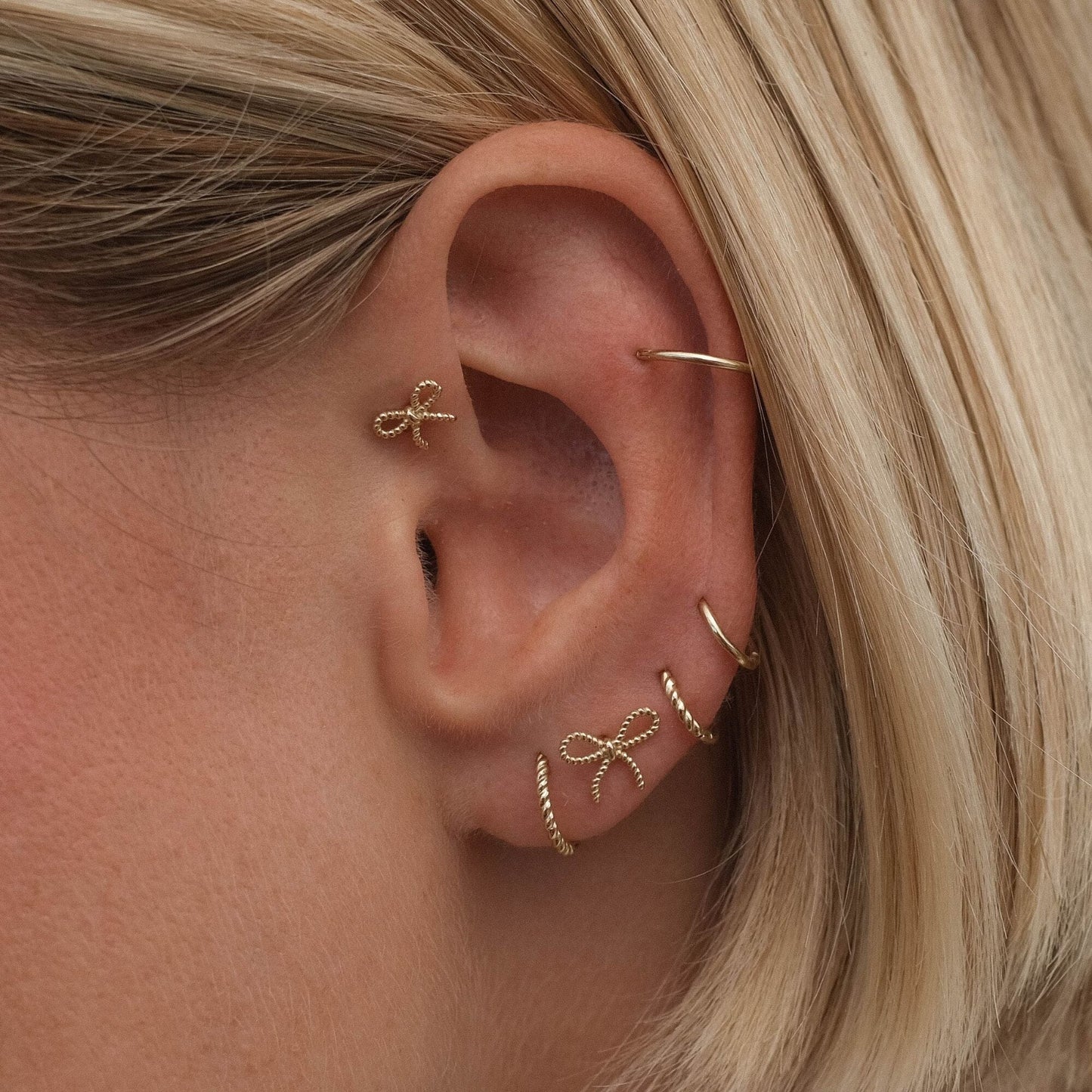 Close-up of a delicate earring set displayed on an ear, showcasing multiple elegant designs with a modern and sophisticated look.