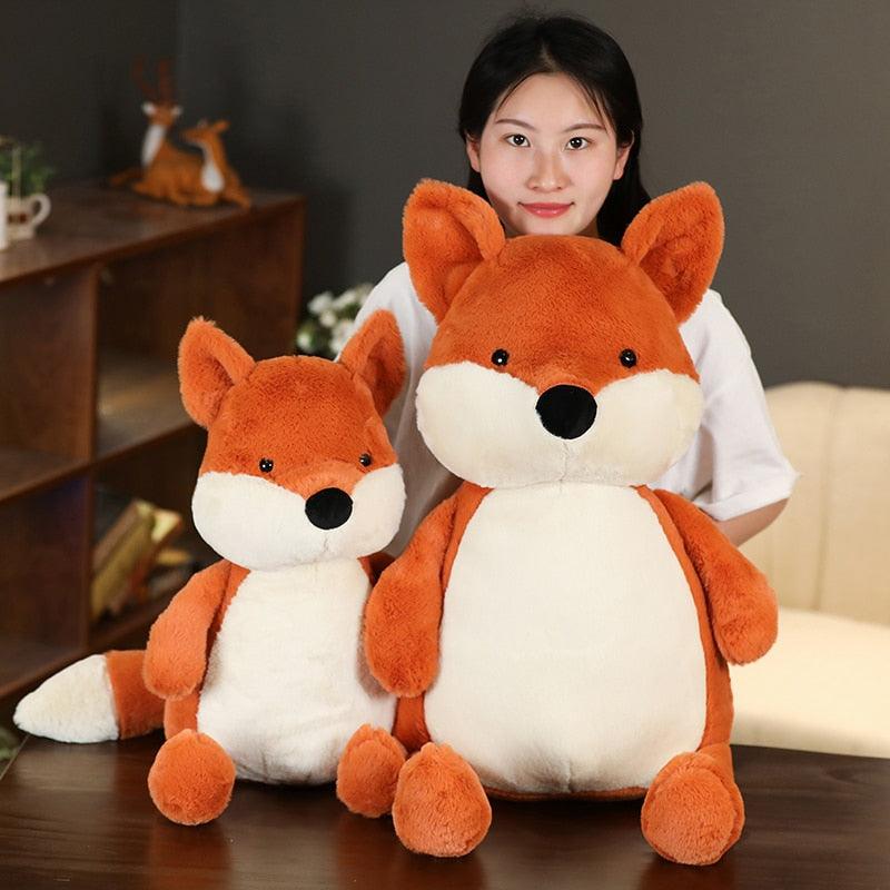 Plush toy set featuring a family of foxes in various sizes, arranged on a cozy bed in a warm and inviting room setting.