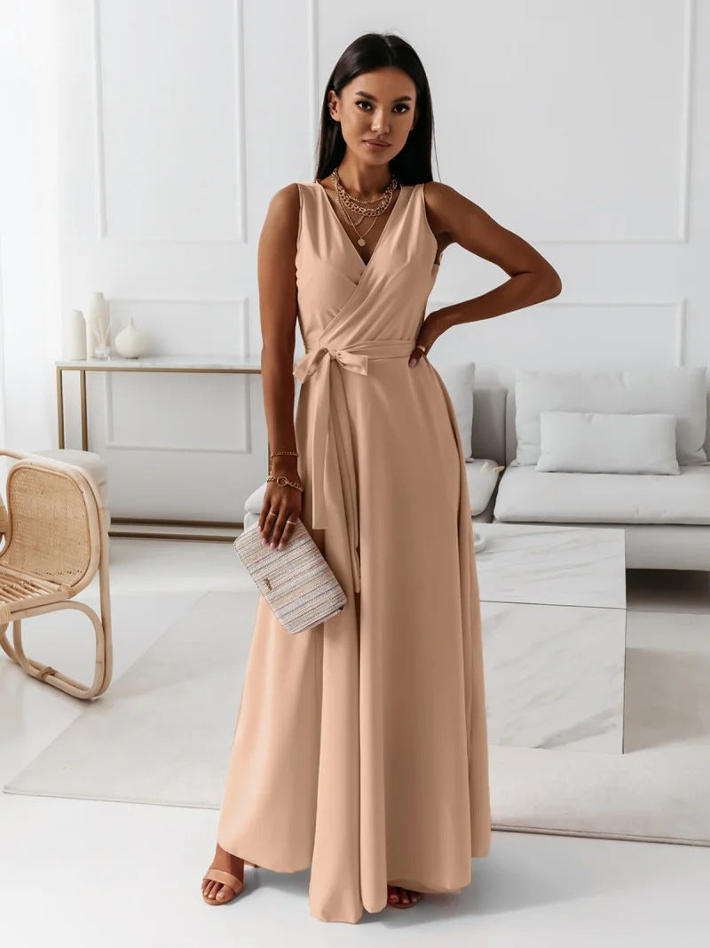 A woman elegantly dressed in a wrap maxi dress featuring a flowing design, styled with minimal accessories, holding a clutch bag, and posing gracefully in a modern living space.