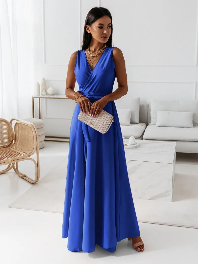 A woman elegantly dressed in a wrap maxi dress featuring a flowing design, styled with minimal accessories, holding a clutch bag, and posing gracefully in a modern living space.