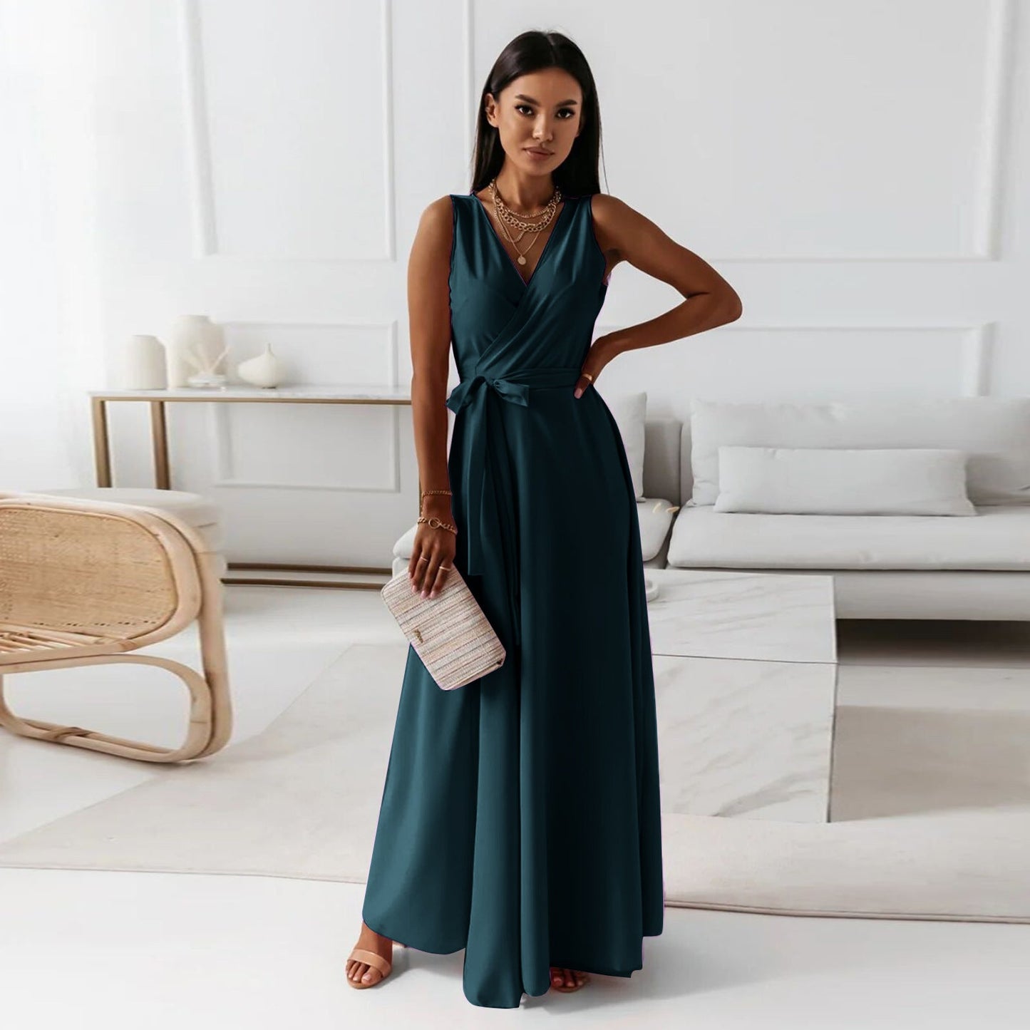 A woman elegantly dressed in a wrap maxi dress featuring a flowing design, styled with minimal accessories, holding a clutch bag, and posing gracefully in a modern living space.