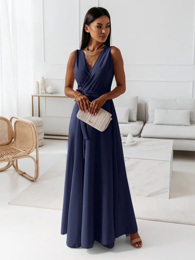 A woman elegantly dressed in a wrap maxi dress featuring a flowing design, styled with minimal accessories, holding a clutch bag, and posing gracefully in a modern living space.