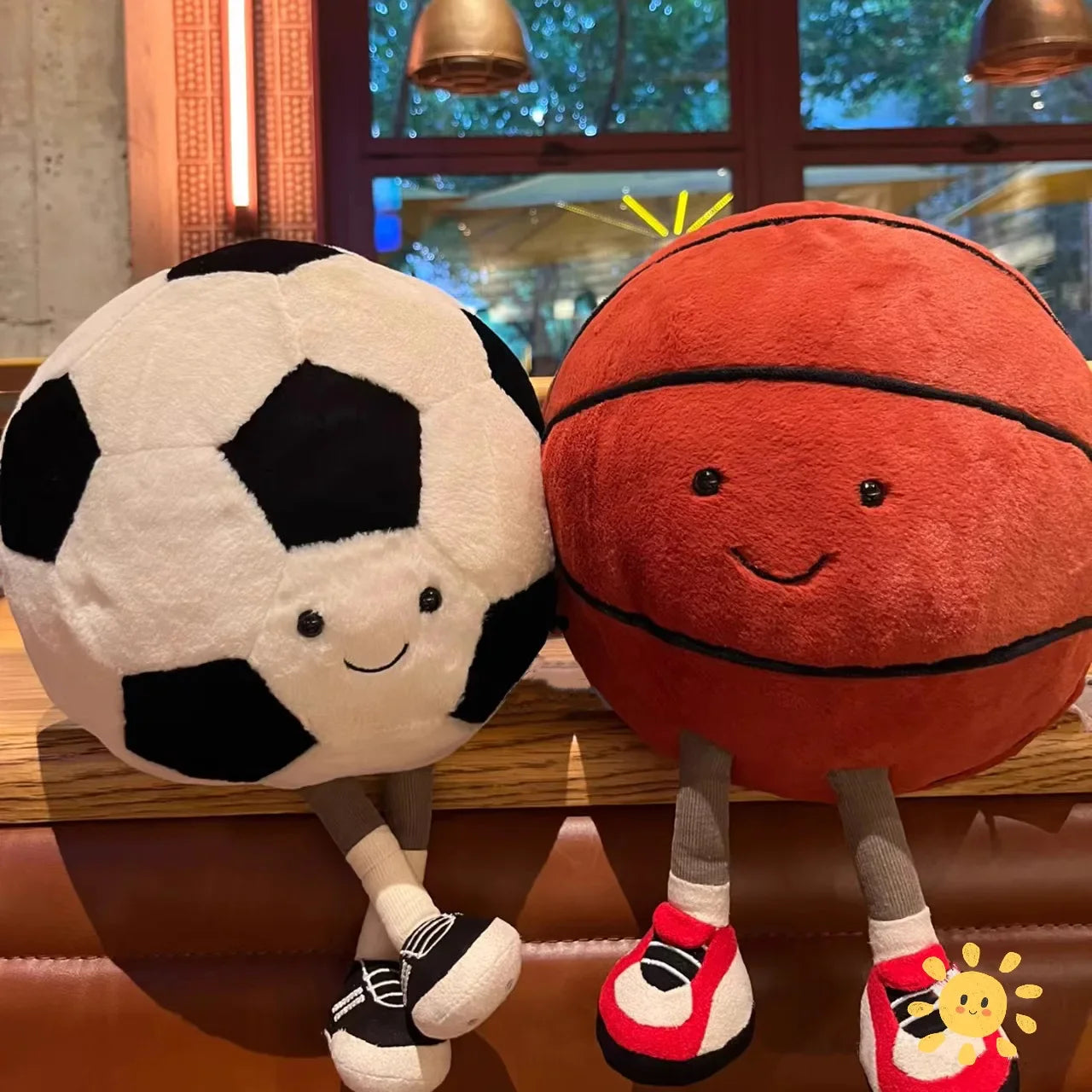Two playful plush toys designed as cheerful companions, featuring unique sports-inspired designs with smiling faces, seated on a cozy surface.