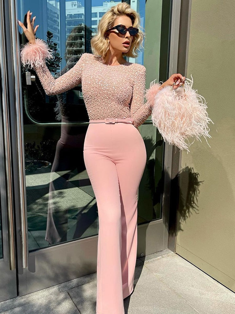 A stylish woman wearing an elegant sequined jumpsuit with a fitted silhouette, featuring feathered sleeve accents and a belted waist, perfect for glamorous events or formal occasions.