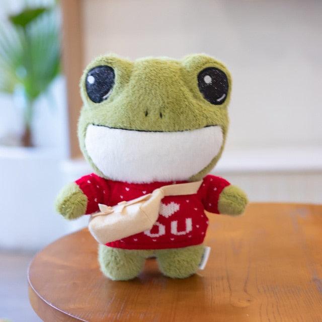 Adorable plush frog toy with a charming design, featuring a small bag and decorative details, placed on a wooden surface.