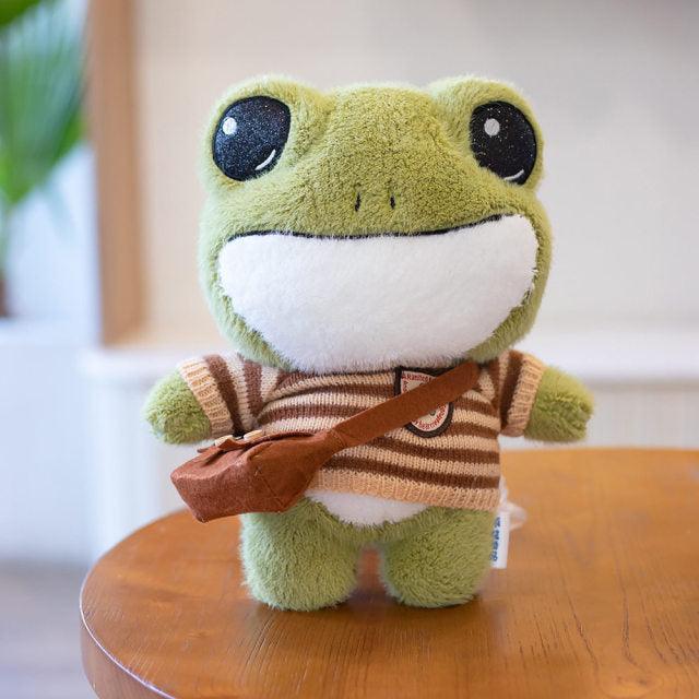 Adorable plush frog toy with a charming design, featuring a small bag and decorative details, placed on a wooden surface.