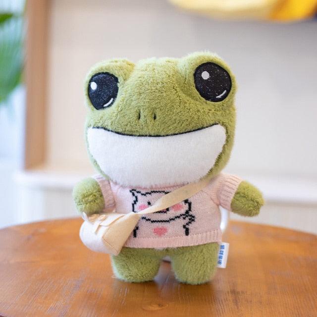 Adorable plush frog toy with a charming design, featuring a small bag and decorative details, placed on a wooden surface.