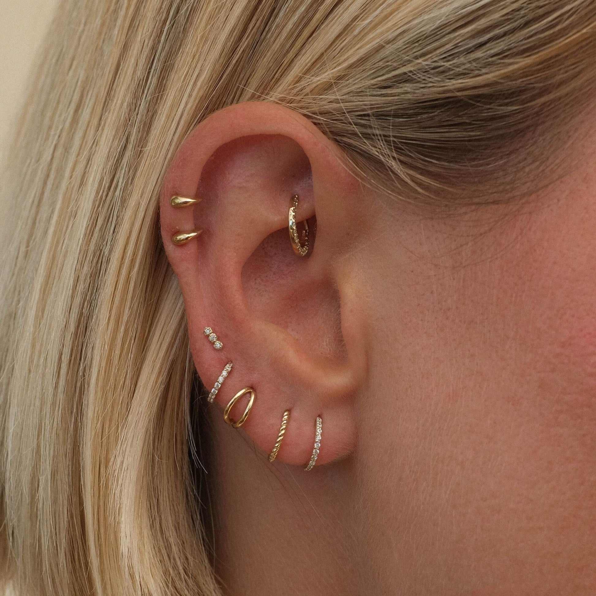 Close-up of a delicate earring set displayed on an ear, showcasing multiple elegant designs with a modern and sophisticated look.