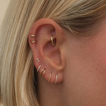 Close-up of a delicate earring set displayed on an ear, showcasing multiple elegant designs with a modern and sophisticated look.