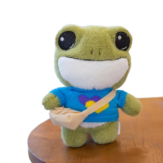 Adorable plush frog toy with a charming design, featuring a small bag and decorative details, placed on a wooden surface.