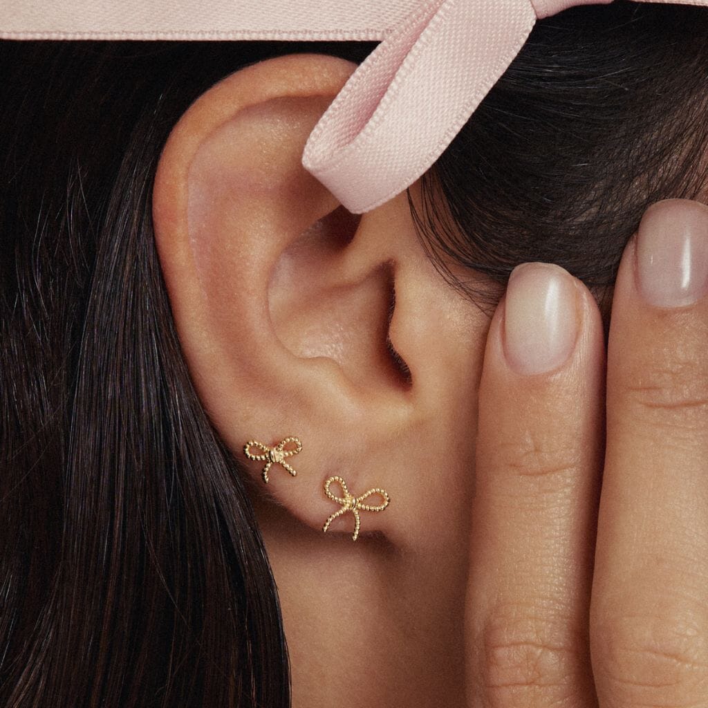Close-up of a woman's ear adorned with delicate bow-shaped earrings, styled with a ribbon in her hair for an elegant and feminine look.