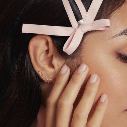 Close-up of a woman's ear adorned with delicate bow-shaped earrings, styled with a ribbon in her hair for an elegant and feminine look.