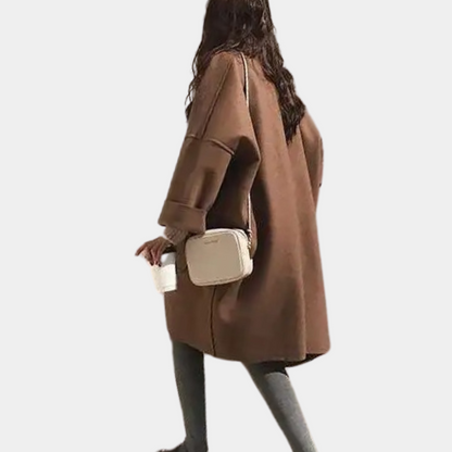 Stylish oversized women's coat with a relaxed fit, featuring deep pockets and a cozy design, worn by a model holding a cup while walking gracefully.