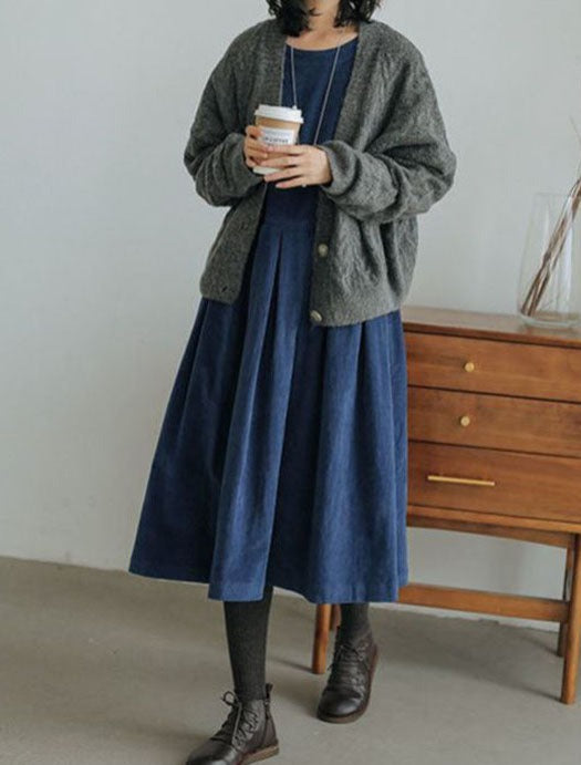 A woman sitting on a wooden chair wearing a vintage midi dress with an elegant design, styled with ankle boots and a long necklace.