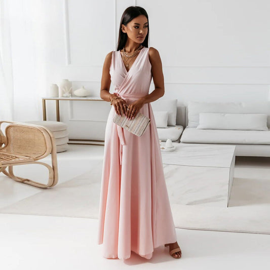  A woman elegantly dressed in a wrap maxi dress featuring a flowing design, styled with minimal accessories, holding a clutch bag, and posing gracefully in a modern living space.