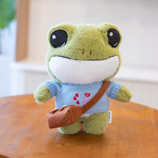 Adorable plush frog toy with a charming design, featuring a small bag and decorative details, placed on a wooden surface.